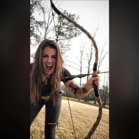 Laura Zerra poses with a bow at a forest.
