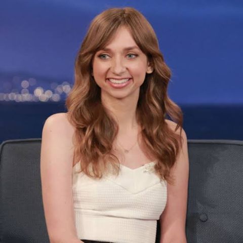 Lauren Lapkus in a white dress poses at an interview.
