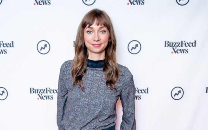 Lauren Lapkus in a grey sweater poses at an event.