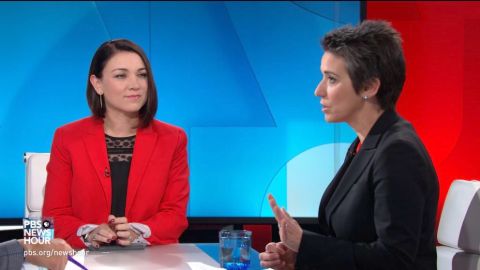 Tamara Keith  in a red coat caught in the camera alongside a co-host.