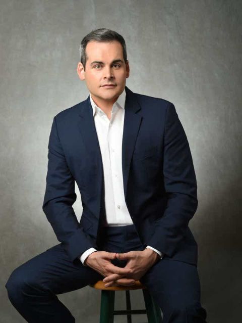 David Begnaud in a black suit poses for a picture.