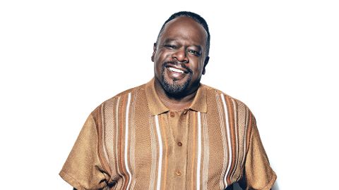 Cedric the Entertainer in a brown t-shirt poses for a picture.