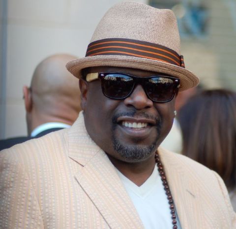 Cedric the Entertainer in a brown coat poses for a picture.