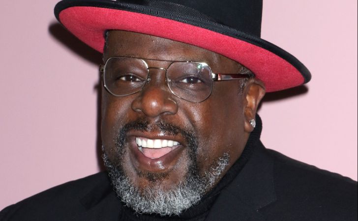 Cedric the Entertainer in a black coat poses for a picture.